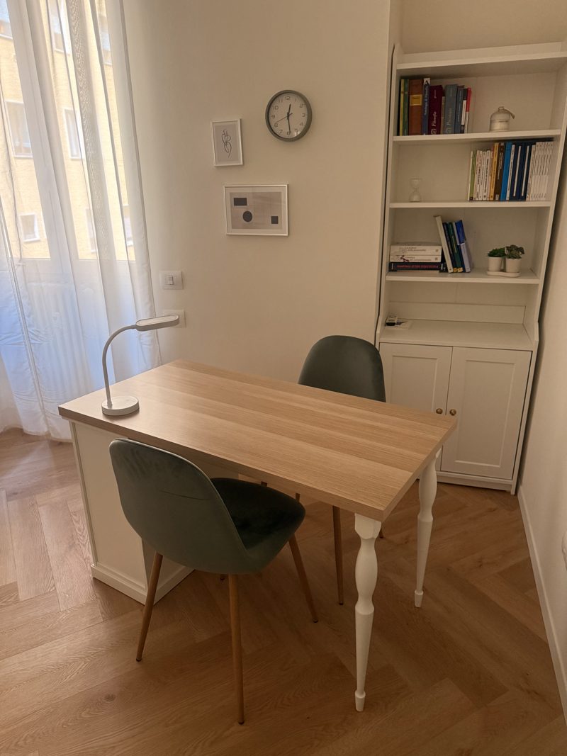 Lo studio di psicologia a Milano: scrivania in legno chiaro con due sedie e una libreria bianca